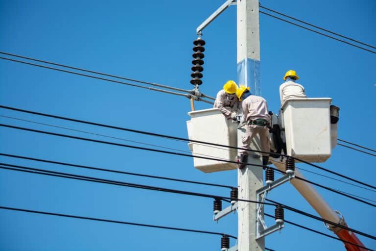 Multiple men in bucket lifts, working on an electrical pole; emphasizing the need for construction labor productivity